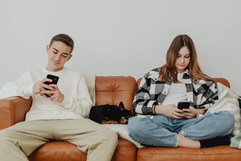 Mexico Tells Tech Platforms to Shield Minors From Harmful Content Two teenagers sitting on a sofa at home using smartphones with a dog